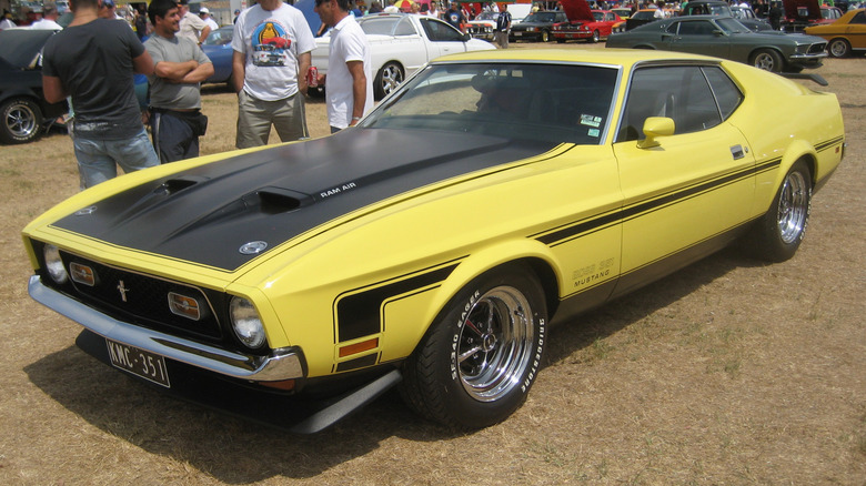 A yellow 1971 Ford Mustang Boss 351 parked on brown grass at a car show