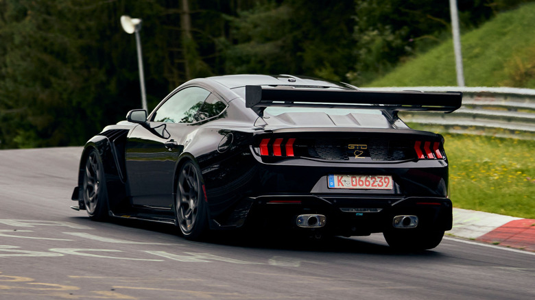 A rear three-quarter shot of a black Ford Mustang GTD accelerating on the Nürburgring
