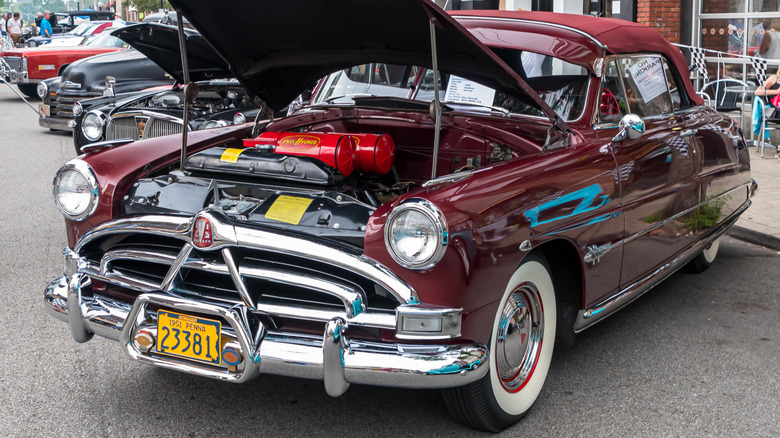 A red Hudson Hornet with its hood open at a car show.