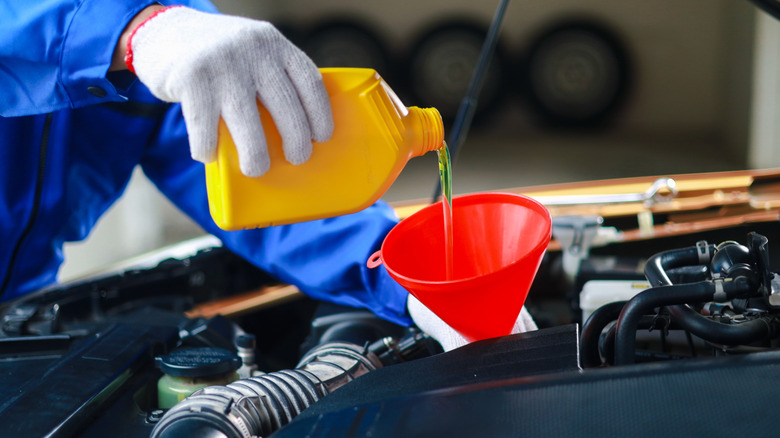 A mechanic pours engine oil into a car through a red funnel.