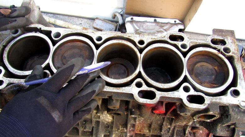 A Volvo five-cylinder engine without the head sitting on a workbench, gloved hands and toothbrush resting on top.