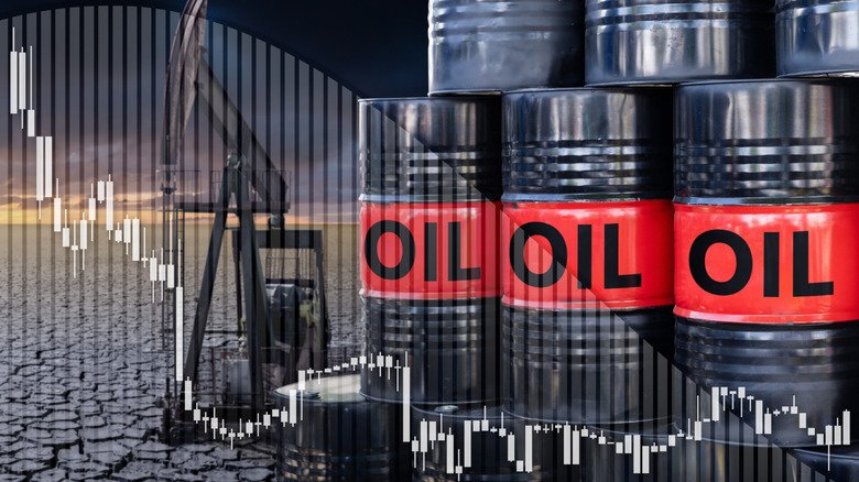 Stacked oil barrels, and an oil derrick in the background of a chart indicating lower production.
