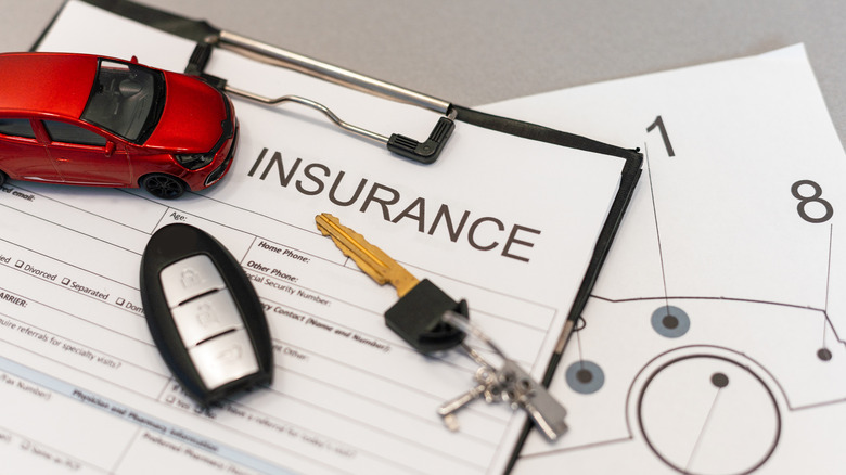 A red miniature car, car and key fob placed on a contract document held in place by a clipboard