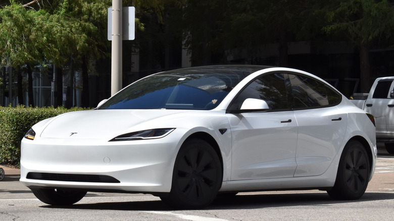 A front left 3/4 of a white Tesla Model 3 compact EV with black rims