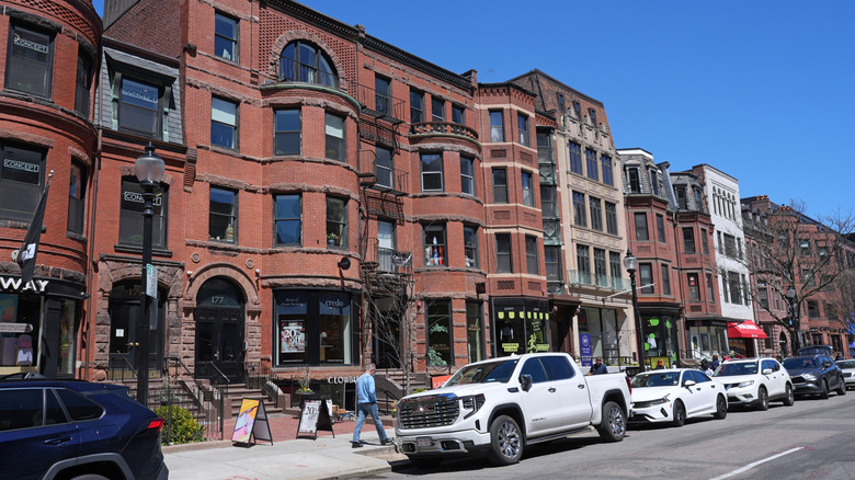 A row of cars parked on the side of the road in front of red brick buildings