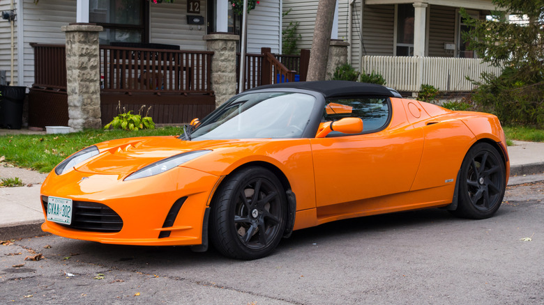 A vright orange original Tesla Roadster parked on a street in front of houses