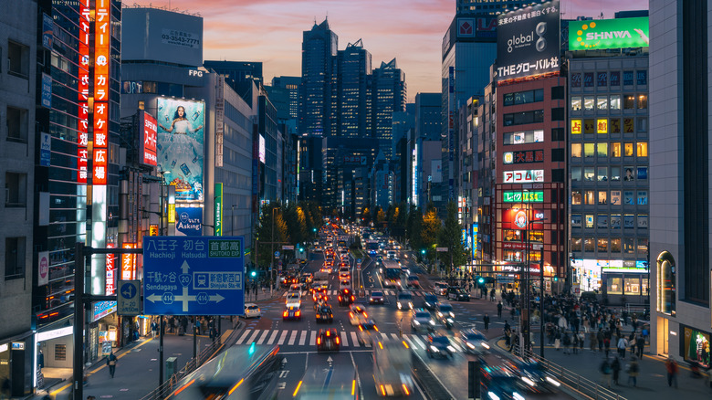 Busy traffic at night in a Japanese city with a line of green lights visible