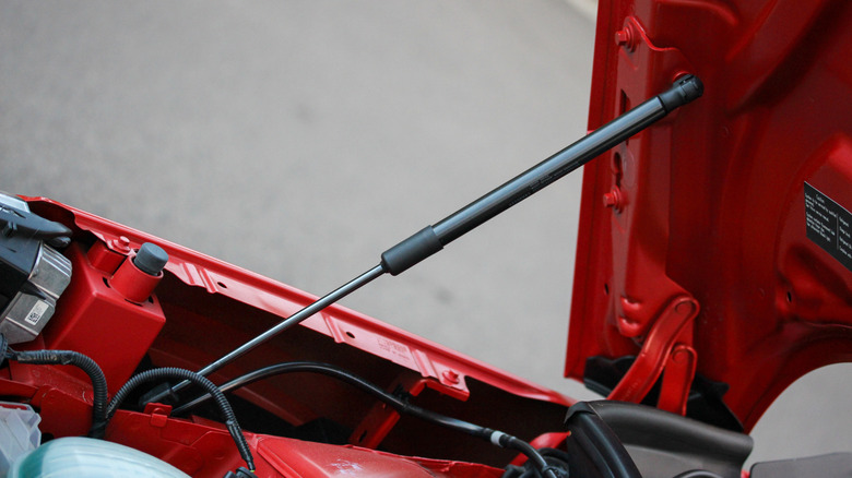A close-up of a gas hood strut on a red car