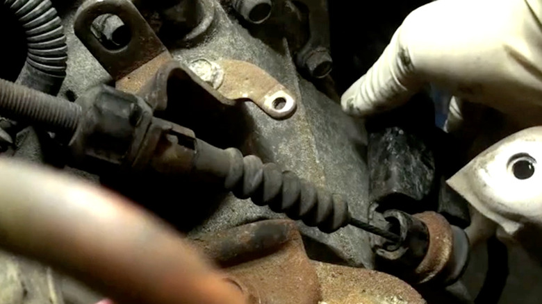 A mechanic adjusts the clutch cable under the hood of a Honda car.