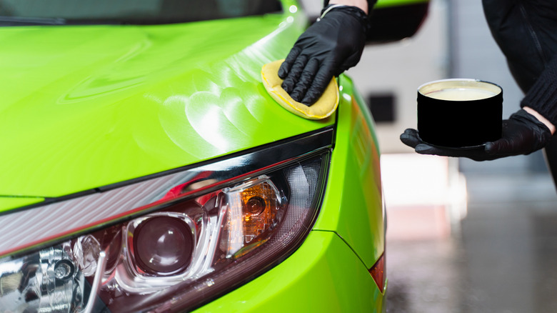 A detailer applying wax to a car's green paint