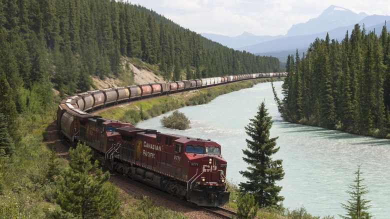 Two diesel electric locomotive hauling a line of freight in a remote landscape alongside a river
