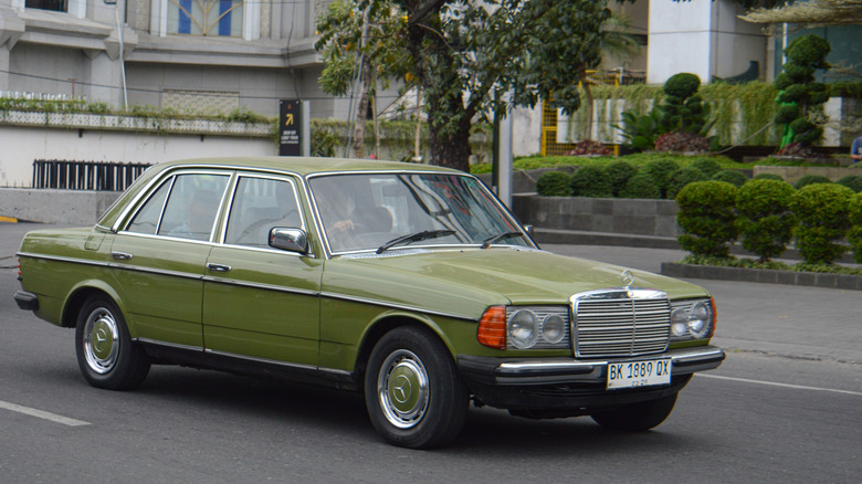 A green W123 Mercedes rolling through a cityscape.