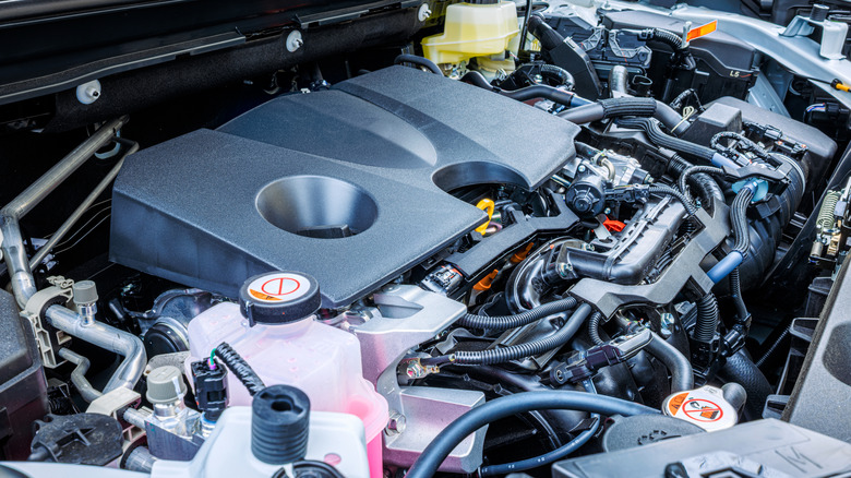 A closeup of a modern gasoline car engine showing large black engine cover, surrounded by engine components