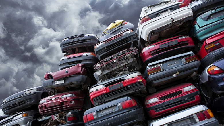 Multiple columns of cars stacked in a junkyard against a gray, overcast sky