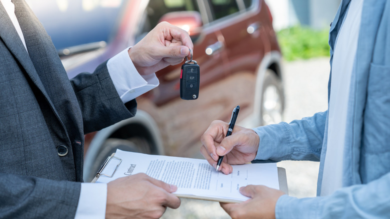 A person being handed the keys to a new car as they are signing the sales contract