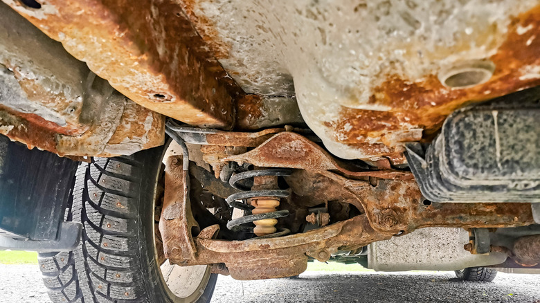 The underside view of a vehicle showing a heavily rusted frame and suspension components