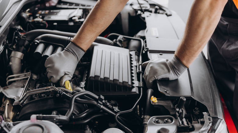 A mechanic wearing gray gloves working on a modern car engine with hands near air filter housing