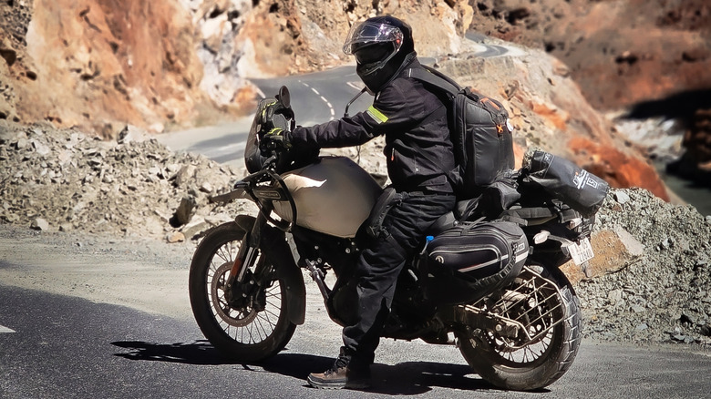 A rider sits on a parked Royal Enfield Himalayan adventure motorcycle on a high-altitude mountain pass.