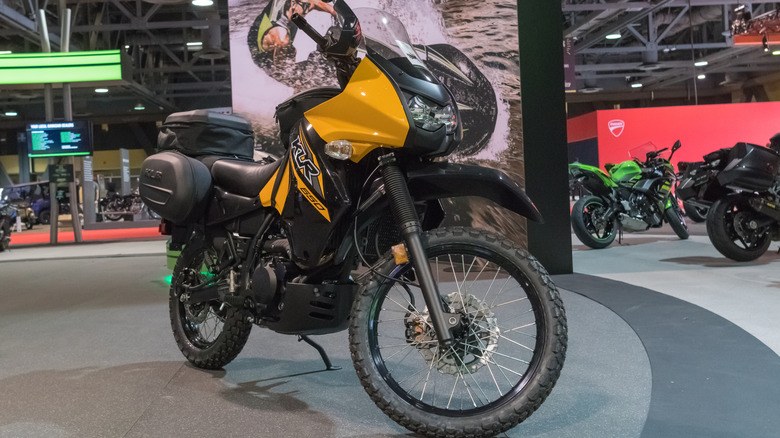 A new black and yellow Kawasaki KLR 650 on a trade show stand with various other bikes in the background