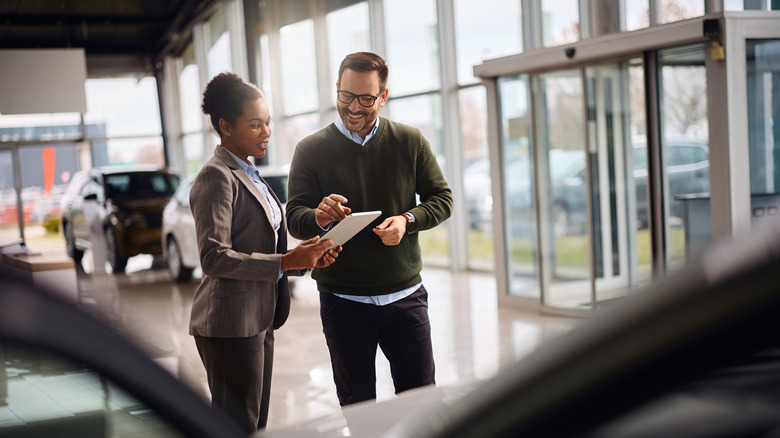 Two people having a conversation and smiling at a car dealership.