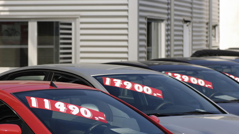 A row of cars with window stickers on them.
