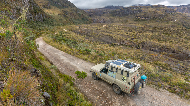 A 60 series Toyota Land Cruiser trekking through mountains on an unpaved road