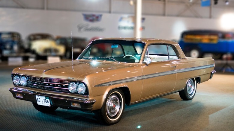 A 1963 model year Oldsmobile Jetfire sitting in beautiful a champagne-like color inside of a museum.