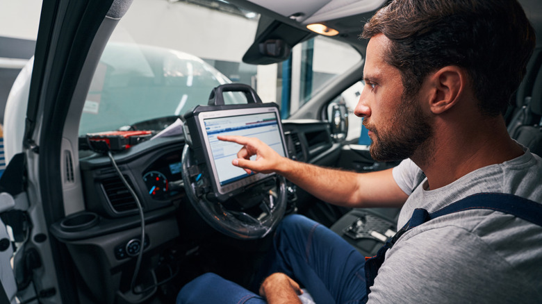An auto repair technician sitting in the driver's seat using a diagnostic computer