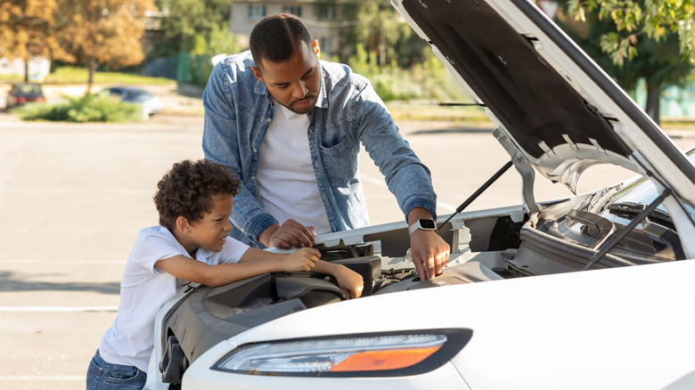 A man showing a young boy under the hood of a car