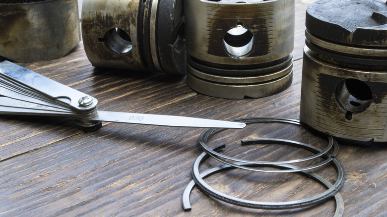 A feeler gauge, pistons, and piston rings, presumably altogether during the assembly on an engine.