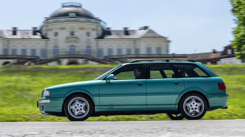 A green Audi RS2 cruising past a beautiful building on a sunny day.