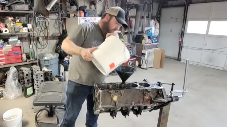 A man pouring block filler into engine block in a garage