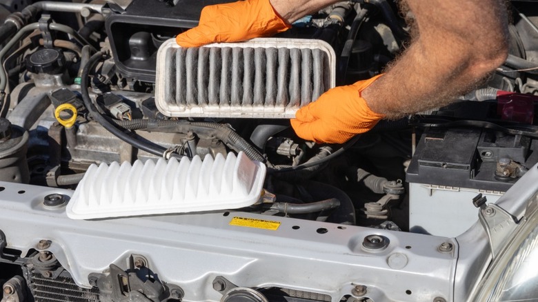 A mechanic in orange gloves replacing the air filter in car
