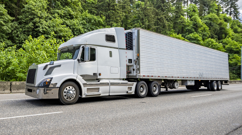 A white semi-truck driving slowly over hilly terrain