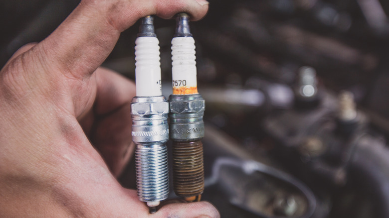 A mechanic holding an old and new spark plug