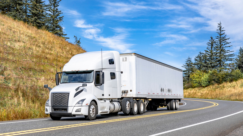 A large, white tractor trailer with a large front grille, on a two-lane road.