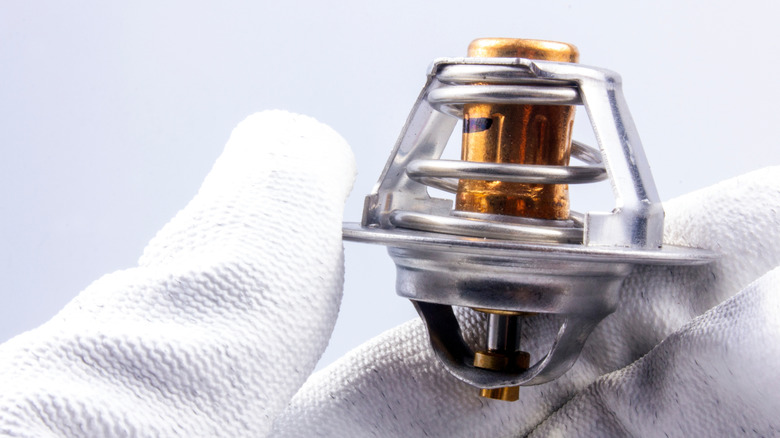 A close look at a car thermostat being held by a hand in a white glove.