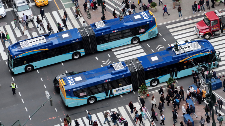Two New York City buses passing each other on a busy street.