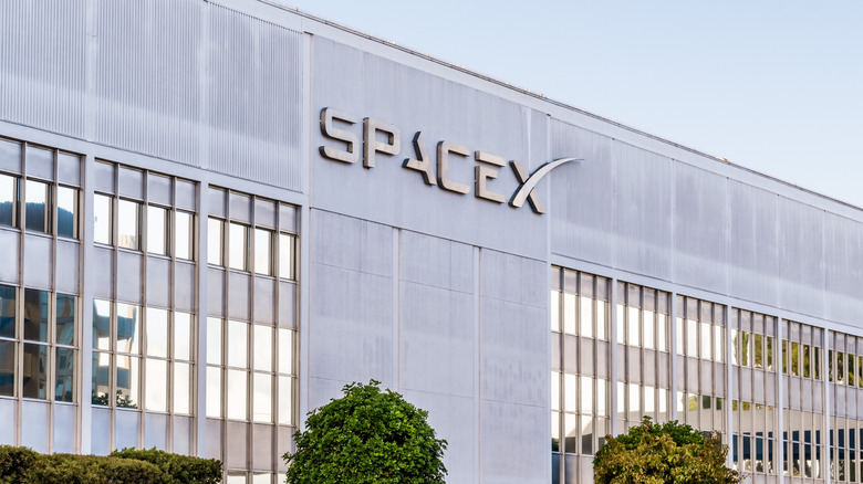 The Space X logo on the side of a company building during the day.