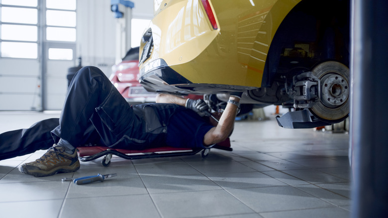 Skilled male mechanic lying down on a creeper, working underneath a car at Auto Repair Shop
