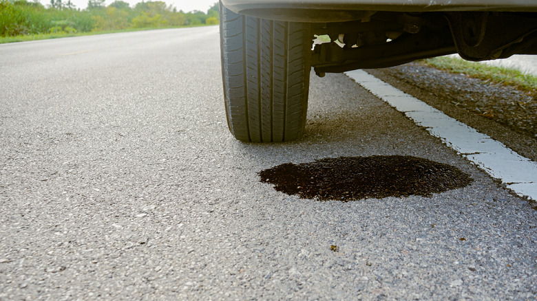 Close-up of dirty engine oil leaking under a broken-down car on the side of the road.