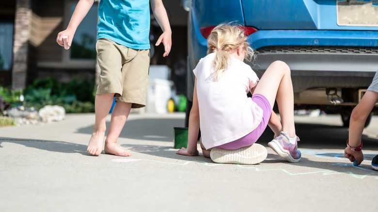 Children sitting on a driveway behind a vehicle in a blind spot.