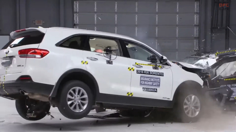 A white 2016 Kia Sorento SUV hitting a 2018 Kia Forte in a head-on collision during an IIHS crash test.