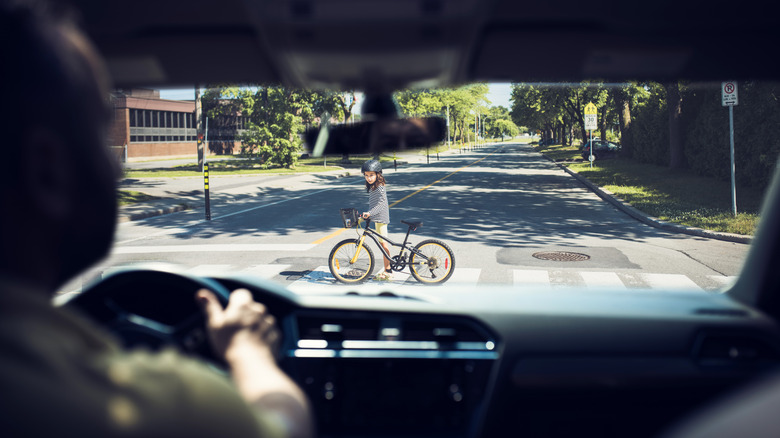 A kid crossing the road with a bike, as seen from inside a car.
