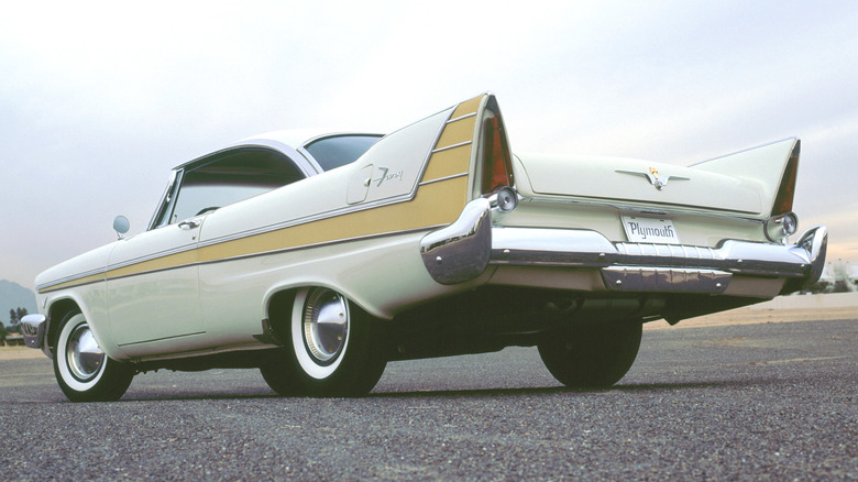A white 1957 Plymouth Fury parked on a paved runway against an overcast sky