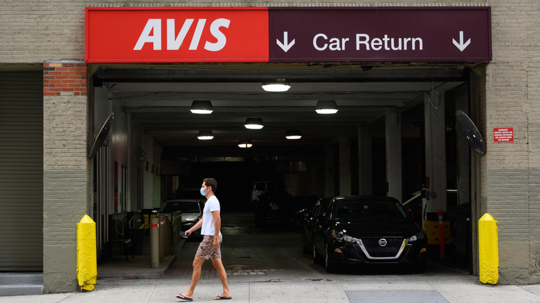 A man walking past an Avis car rental return location in a city