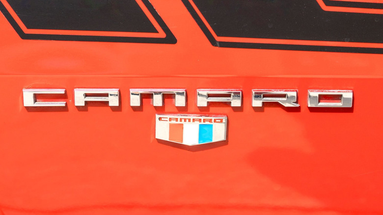 The camaro's "tri-bar" badge with the word "Camaro" above it in silver letters against orange paint