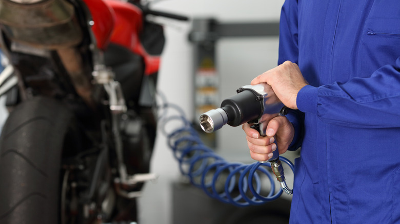 A technician using an air-powered impact wrench on a motorcycle.