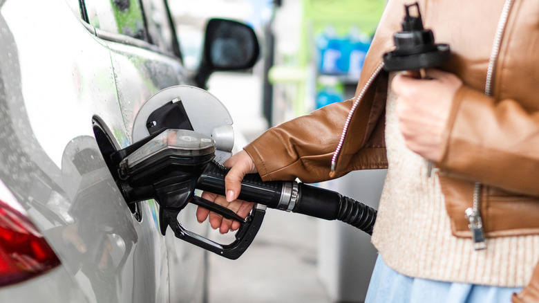 A woman holds a gas pump at a filling station.