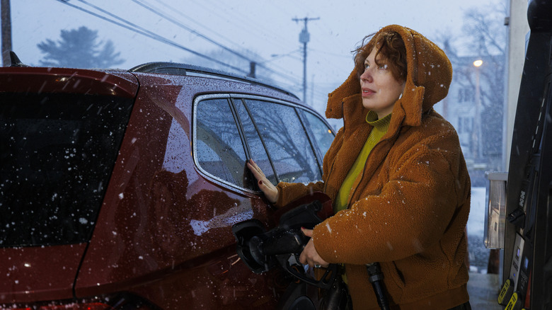 A woman pumps gas in the midst of a snowstorm.